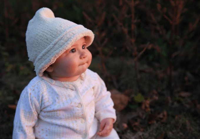 Portrait of a baby looking to the right while wearing a fuzzy white beanie and pink onesie