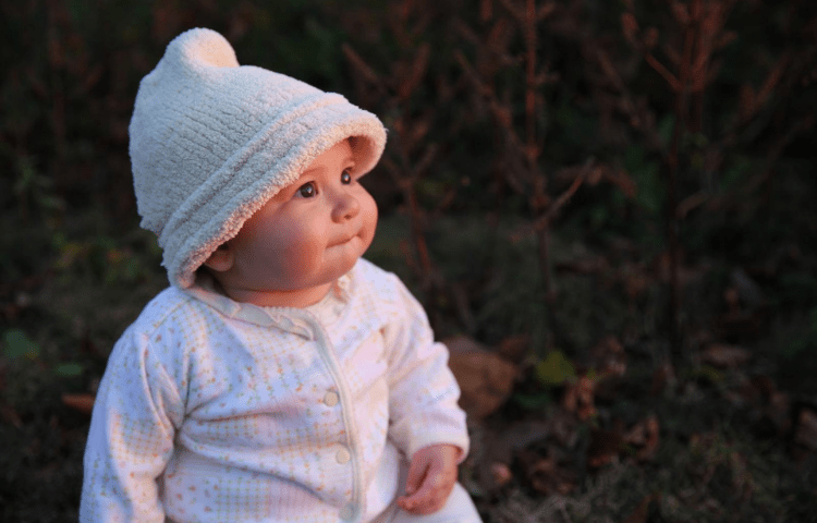 Portrait of a baby looking to the right while wearing a fuzzy white beanie and pink onesie