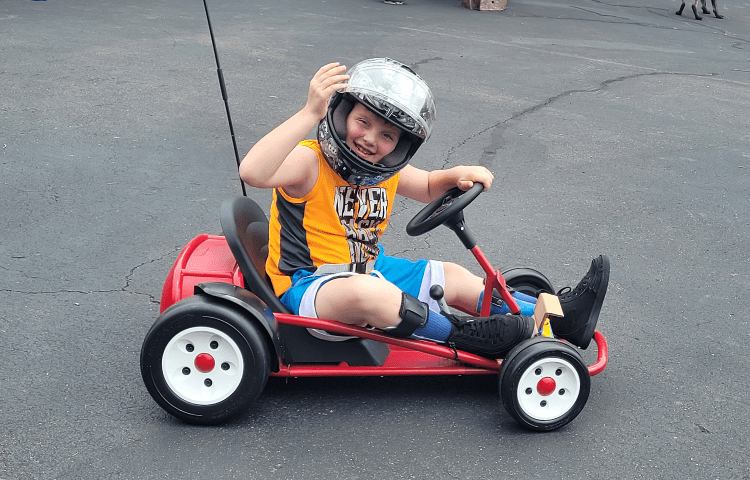 Boy with helmet on smiles and waves for a photo while riding in a go kart