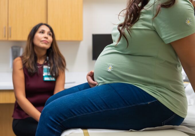 Pregnant woman sits in doctors office while a maternal fetal medicine specialist listens to her questions.
