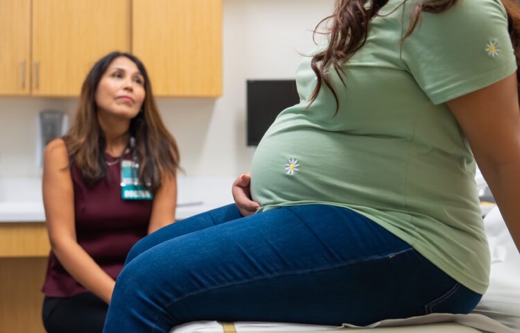 Pregnant woman sits in doctors office while a maternal fetal medicine specialist listens to her questions.