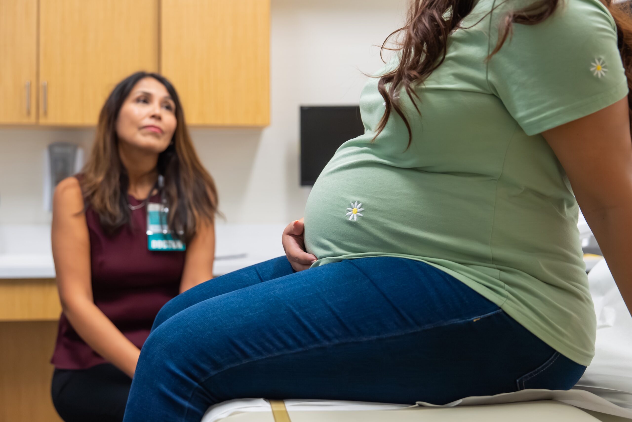 Pregnant woman sits in doctors office while a maternal fetal medicine specialist listens to her questions.