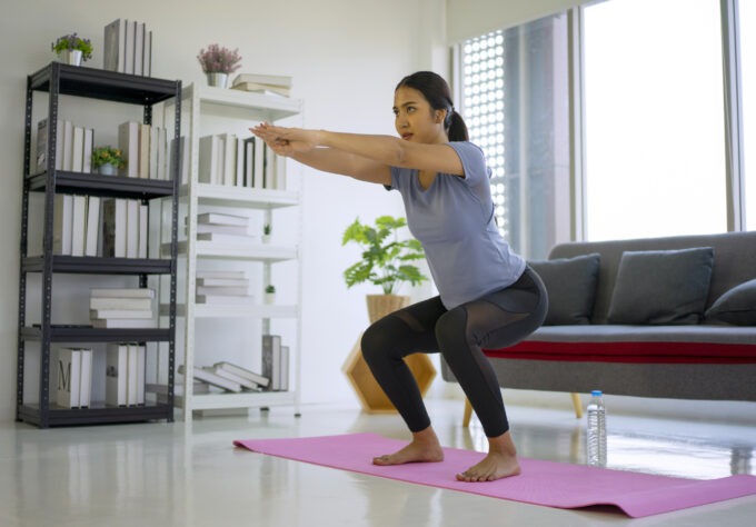 Postpartum mom working out at home by performing a squat exercise.