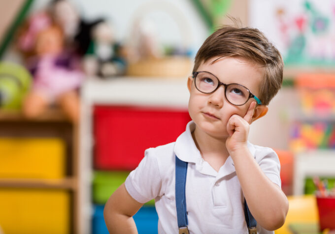 Little boy in glasses and suspenders looking up as if he is pondering something.