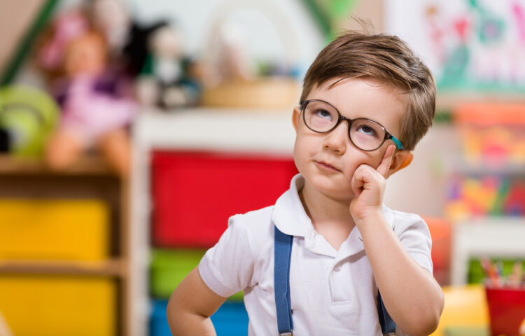 Little boy in glasses and suspenders looking up as if he is pondering something.