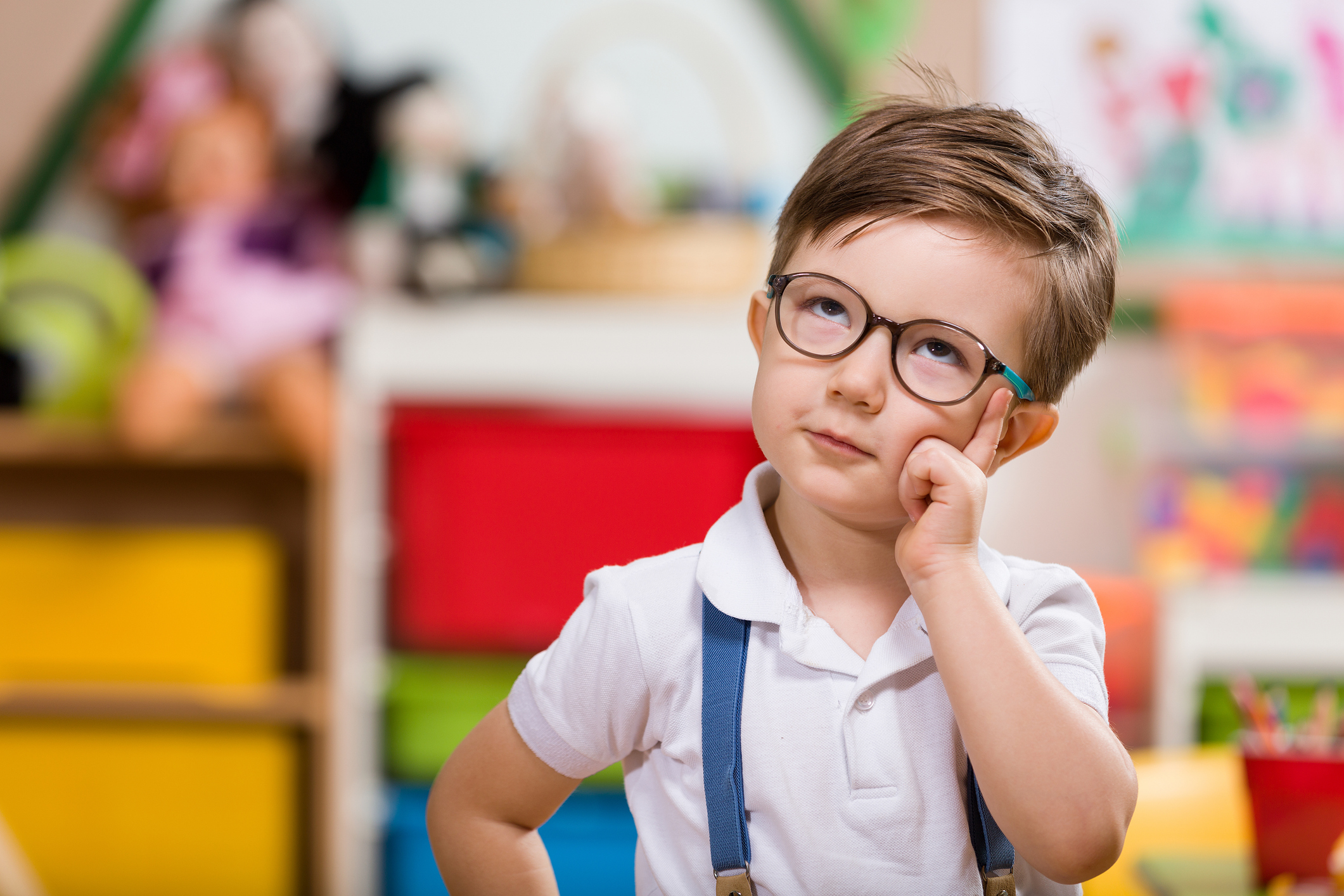 Little boy in glasses and suspenders looking up as if he is pondering something.