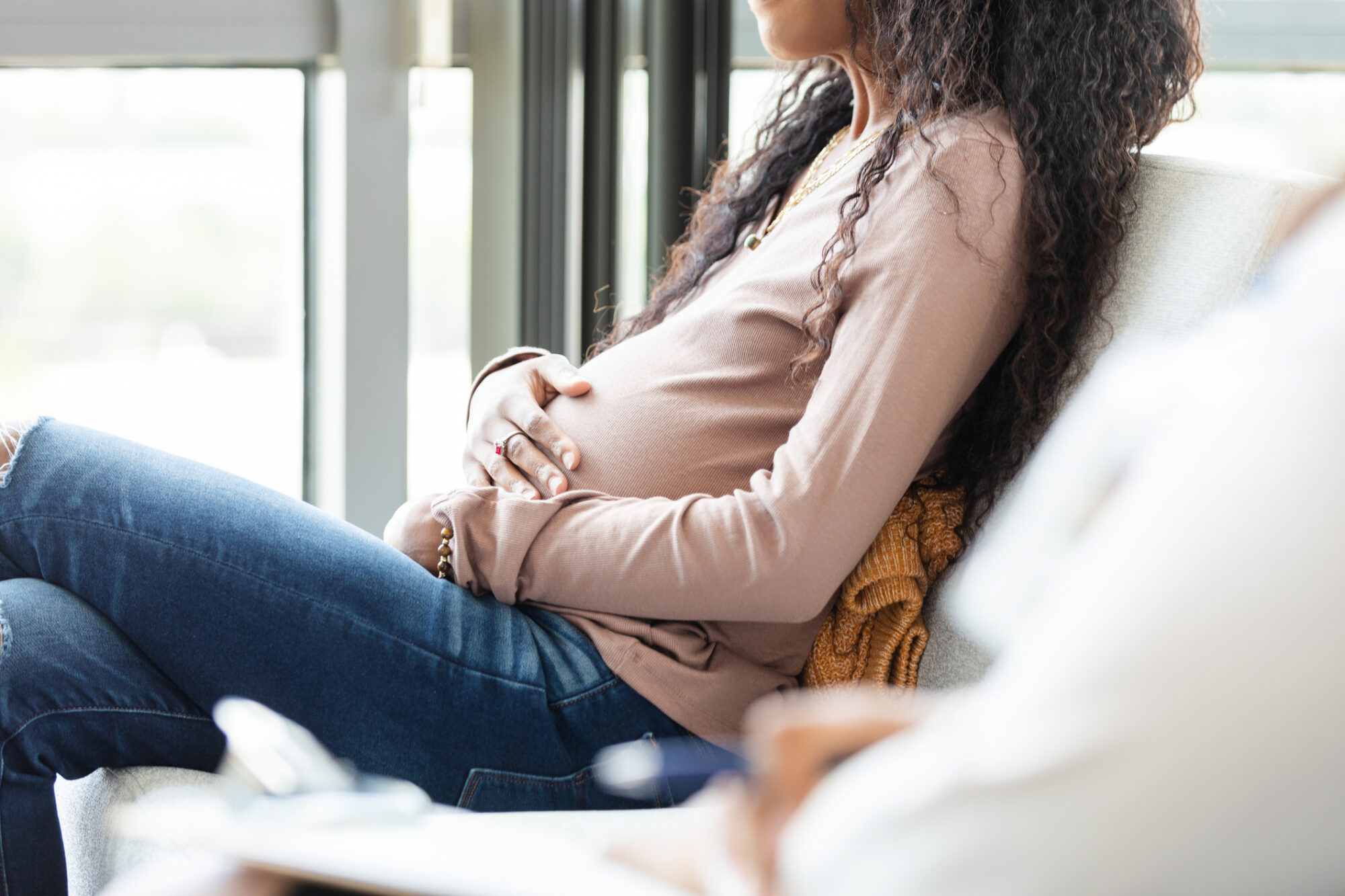 Pregnant woman sitting, gently touching her belly during counseling at a fetal center.