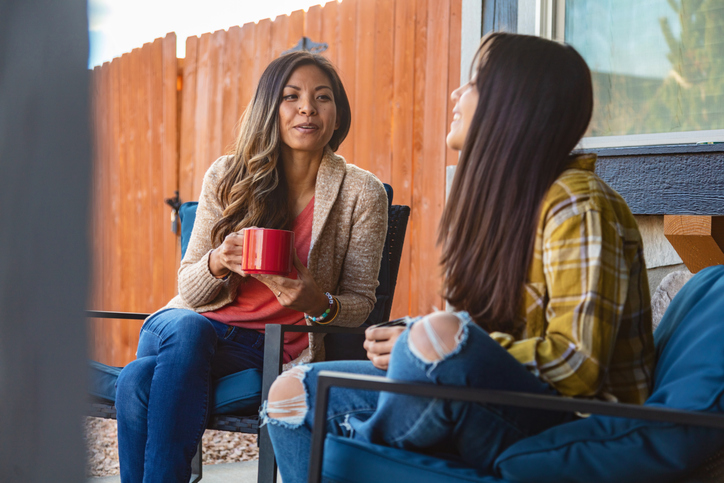 Mother and daughter sitting outside in chairs having a supportive conversation.
