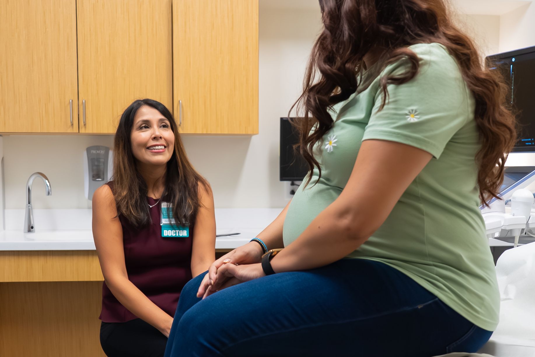 Pregnant woman sits in doctors office while a maternal fetal medicine specialist listens to her questions.
