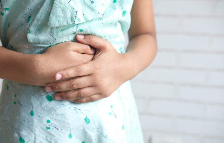 Close up of a girl holding her stomach indicating indigestion.