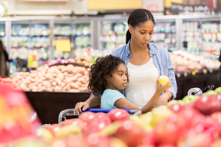 Mom and daughter pick out apples in a grocery store.