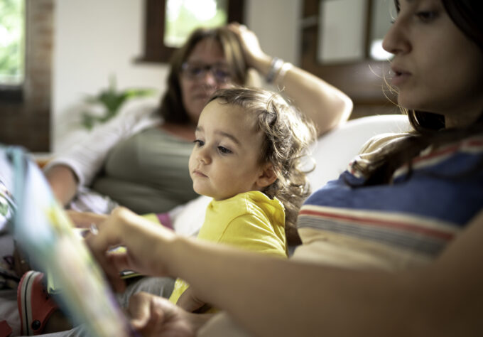 Adult reading a picture book with a young child on a couch, illustrating early literacy development through shared interaction