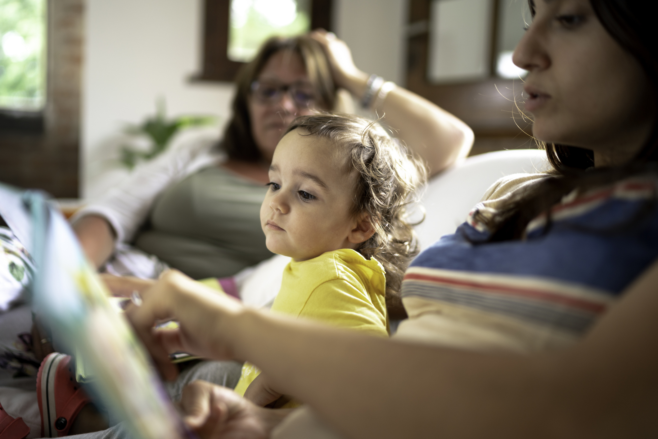 Adult reading a picture book with a young child on a couch, illustrating early literacy development through shared interaction