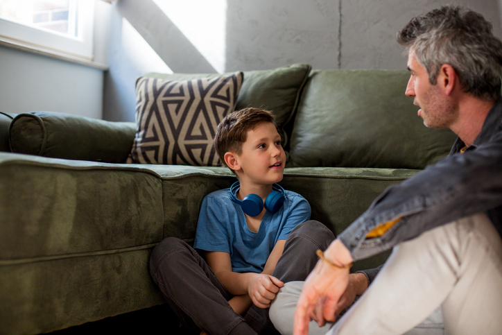 Adult sitting on the floor talking with a young child at eye level, illustrating responsive communication and language development