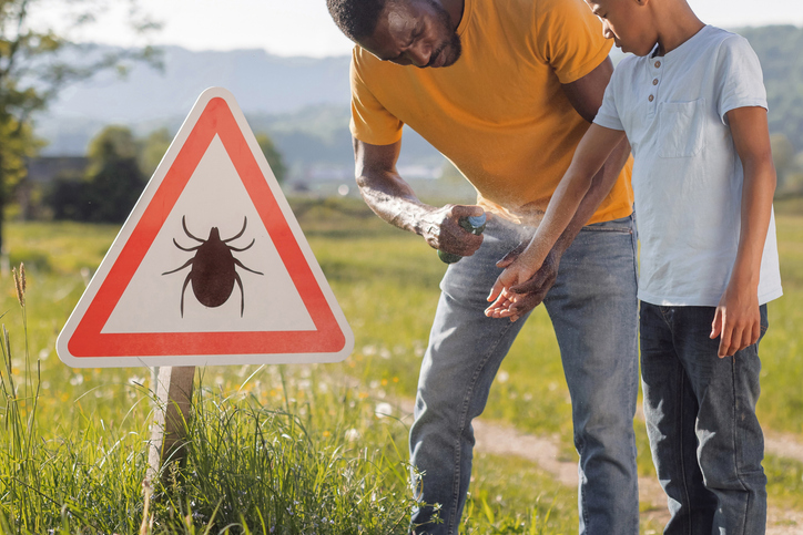 Family notices tick warning sign during hike and applies repellent spray to protect child from tick bites and Lyme disease.