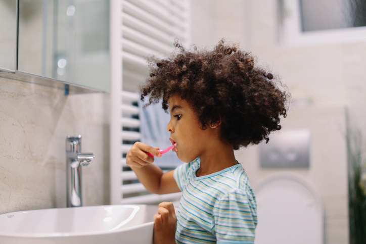 Young child getting ready for school, doing the morning routine in the bathroom. which includes bushing teeth with fluoride toothpaste.
