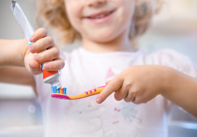 Closeup of little girl putting fluoride toothpaste on a toothbrush.