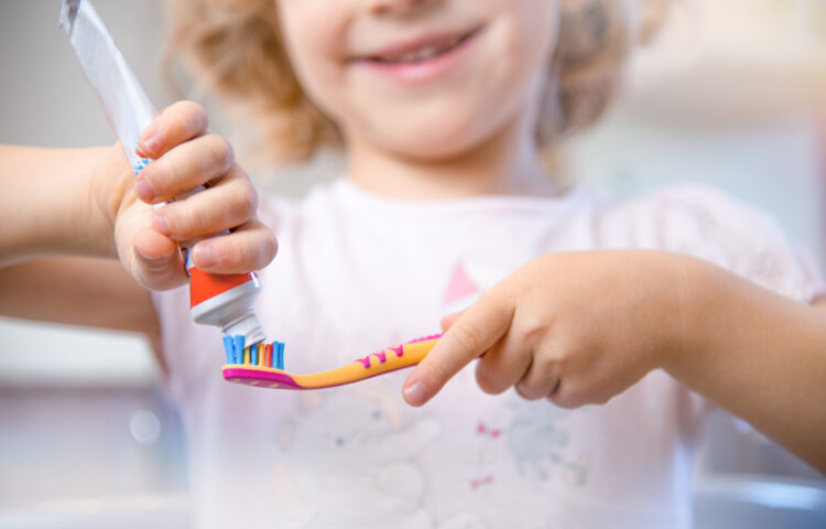 Closeup of little girl putting fluoride toothpaste on a toothbrush.