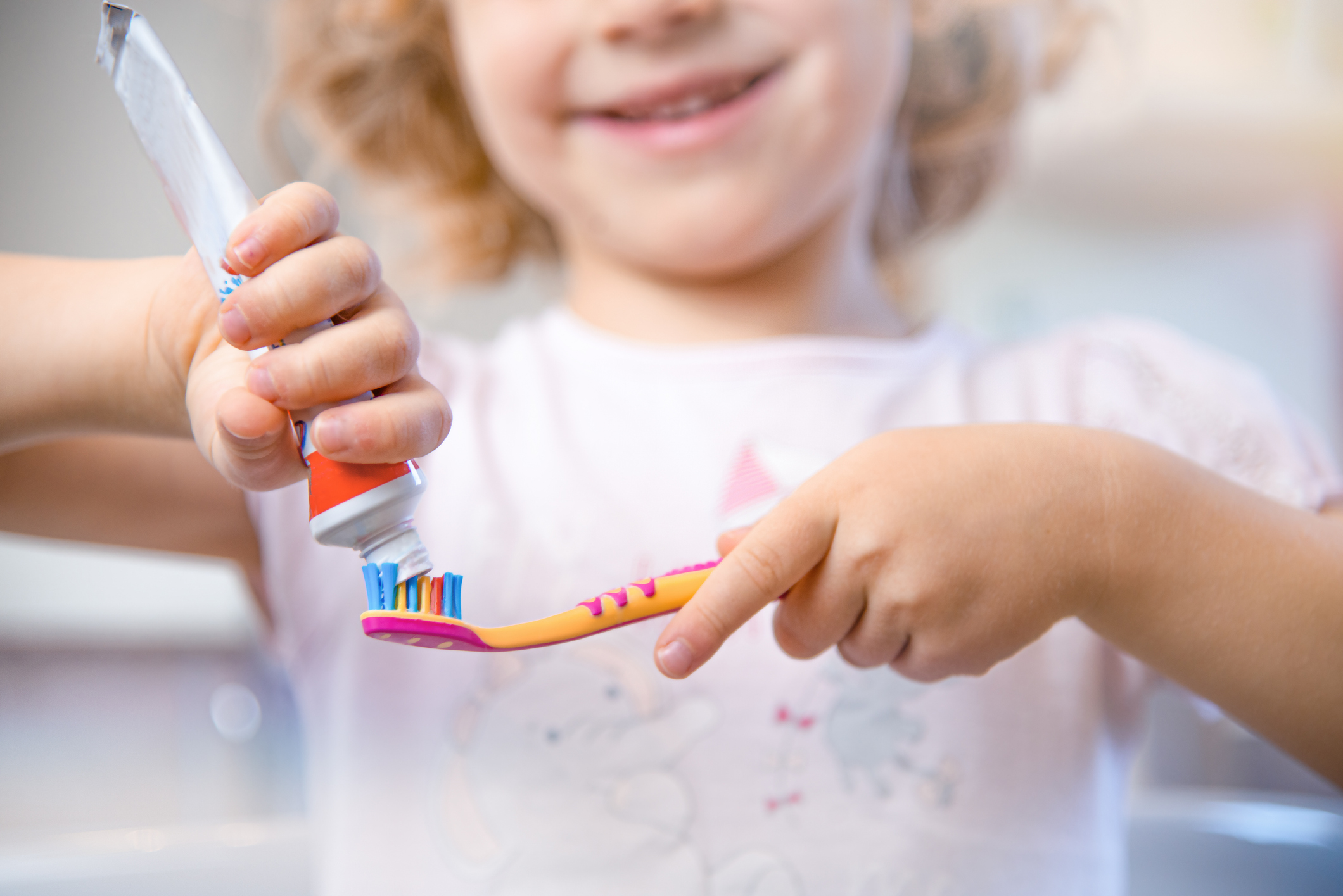 Closeup of little girl putting fluoride toothpaste on a toothbrush.