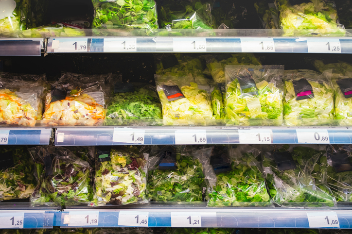 Bags of leafy greens and packaged salads displayed in a grocery store produce section during heightened awareness of Cyclospora contamination risks.