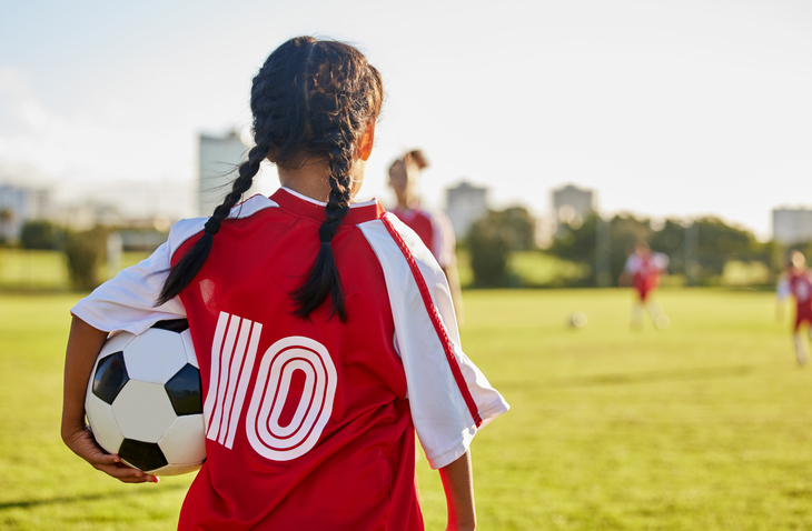 Child holding a soccer ball while standing on a sports field during an outdoor game.