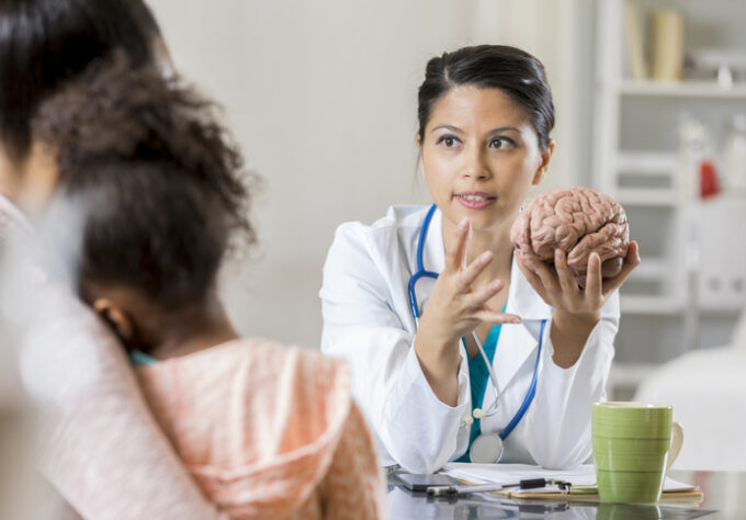 Medical professional using a brain model to explain brain anatomy to a child and caregiver during an office visit.