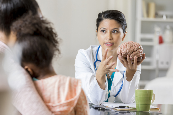 Medical professional using a brain model to explain brain anatomy to a child and caregiver during an office visit.