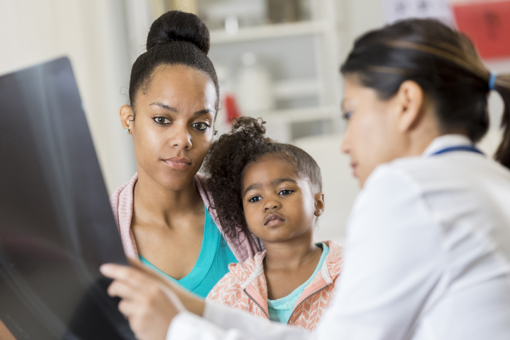 Medical professional reviewing an imaging scan with a child and caregiver during a pediatric consultation.