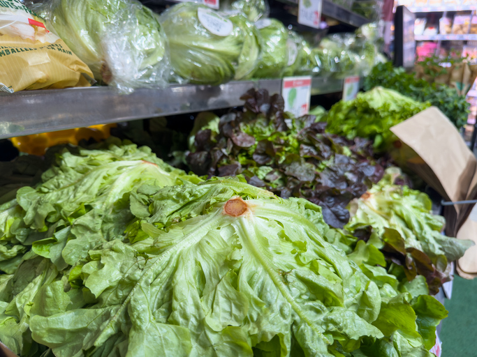 Bags of leafy greens and packaged salads displayed in a grocery store produce section during heightened awareness of Cyclospora contamination risks.