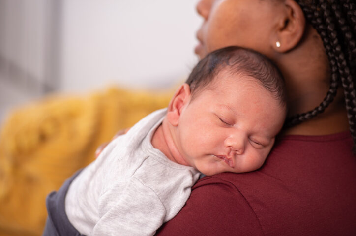 Mother holding a newborn baby and tenderly cuddles gently while the infant is sleepy on the shoulder.