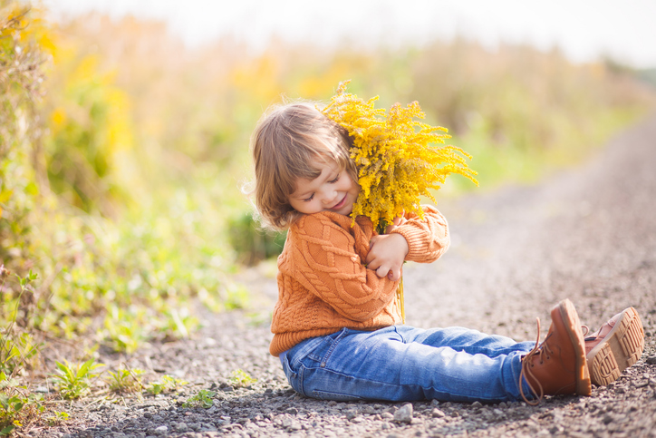 Child sitting outdoors holding a bundle of yellow flowering plants that can be associated with seasonal allergy triggers.
