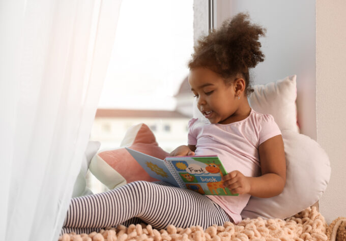 Child sitting with a picture book and exploring early literacy skills through independent reading.