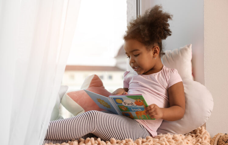 Child sitting with a picture book and exploring early literacy skills through independent reading.