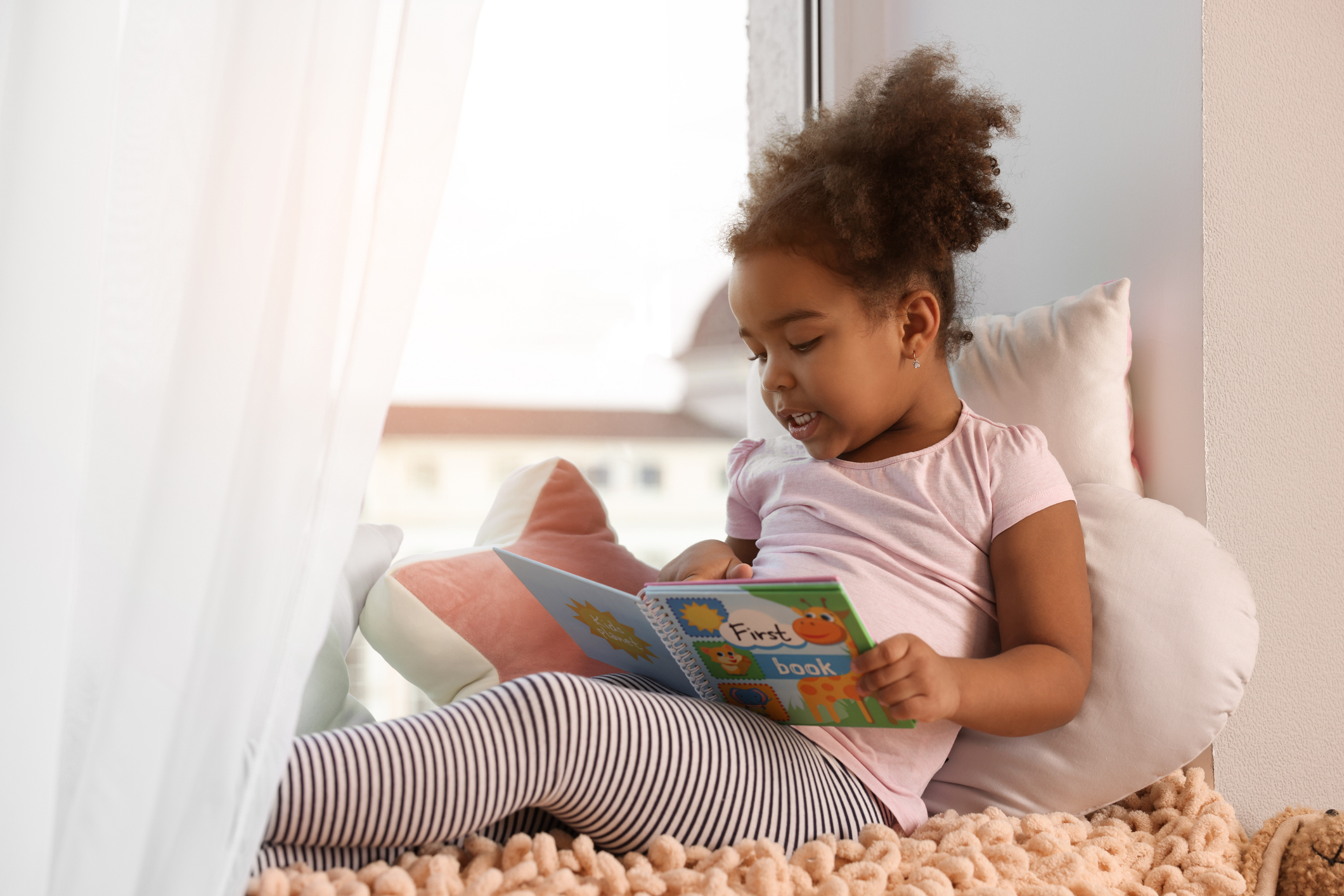 Child sitting with a picture book and exploring early literacy skills through independent reading.