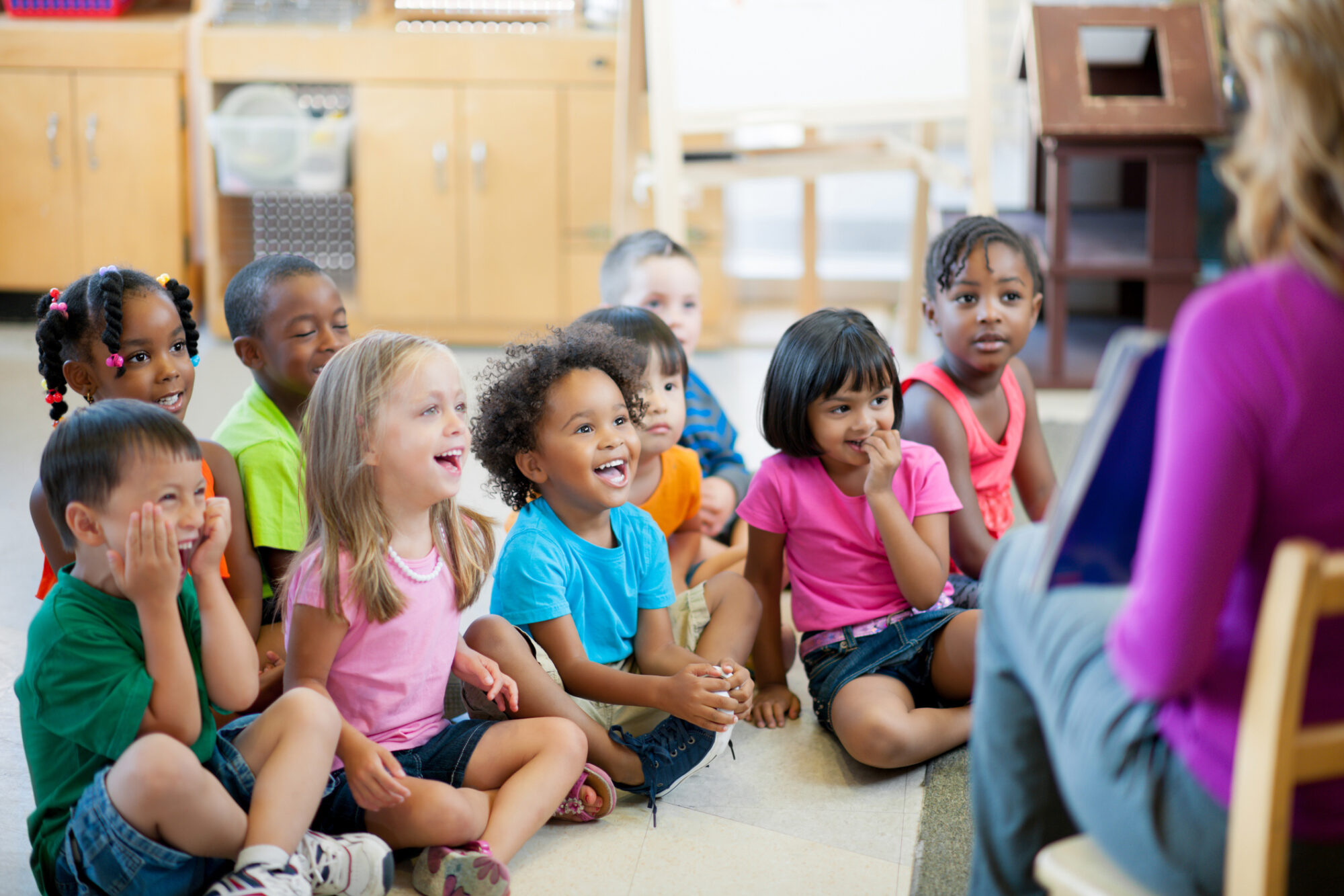 Young children gathered in a classroom group activity, listening to an educator and developing early learning and social skills that support kindergarten readiness.