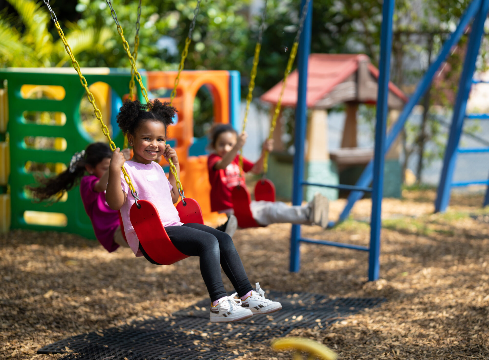 Young children playing on swings at a playground, engaging in physical activity that promotes healthy growth, coordination, and school readiness.