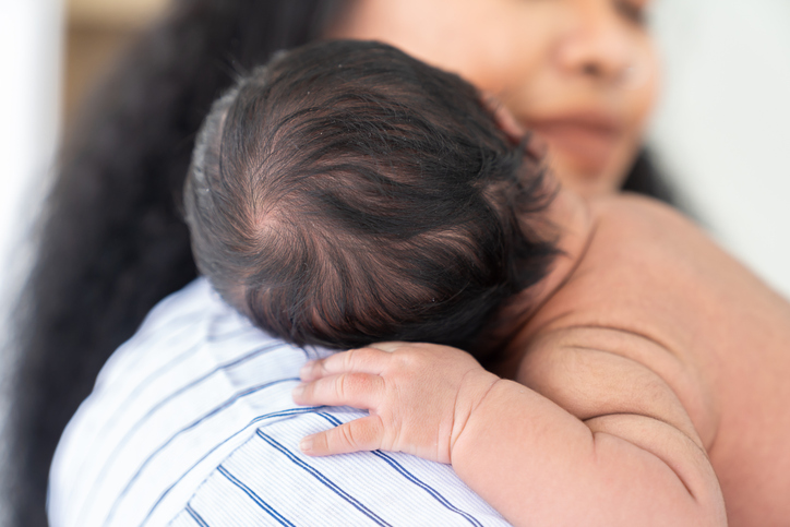 Mother holding a newborn baby with head resting over her shoulder.