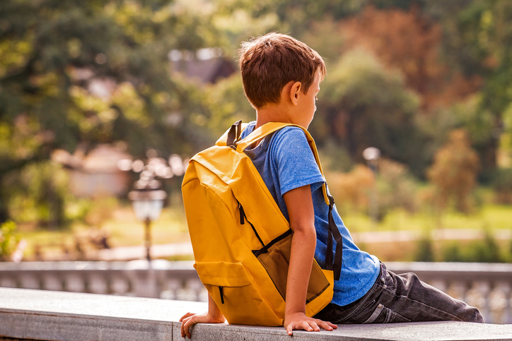 School-age child wearing a backpack outdoors, illustrating the impact of sleep and schedule changes on school readiness.